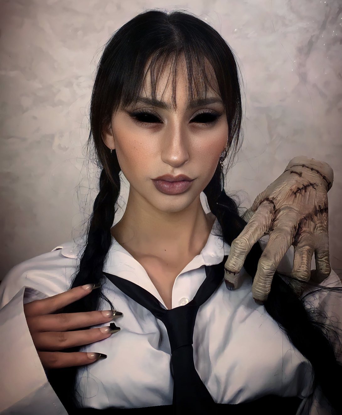 Wednesday-inspired cosplay look with dark eye makeup and a stitched creature hand